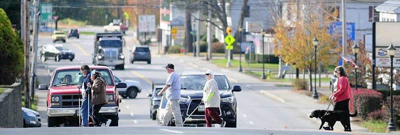 People cross at Bangor Street at the Murray Street intersection during a walk held to raise awareness of white canes and guide dogs today in Augusta.