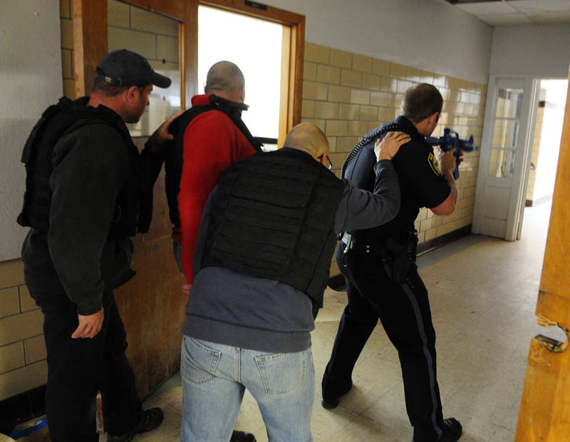 Augusta firefighter/paramedics Shawn Stevens, left, Scott Sirois, wearing a red jacket, and Rich Beaudoin stay low and close to the wall, as they follow Augusta Police patrolman Ben Murtiff down a hallway during a simulated school shooting incident Friday at the former Hodgkins middle school in Augusta.