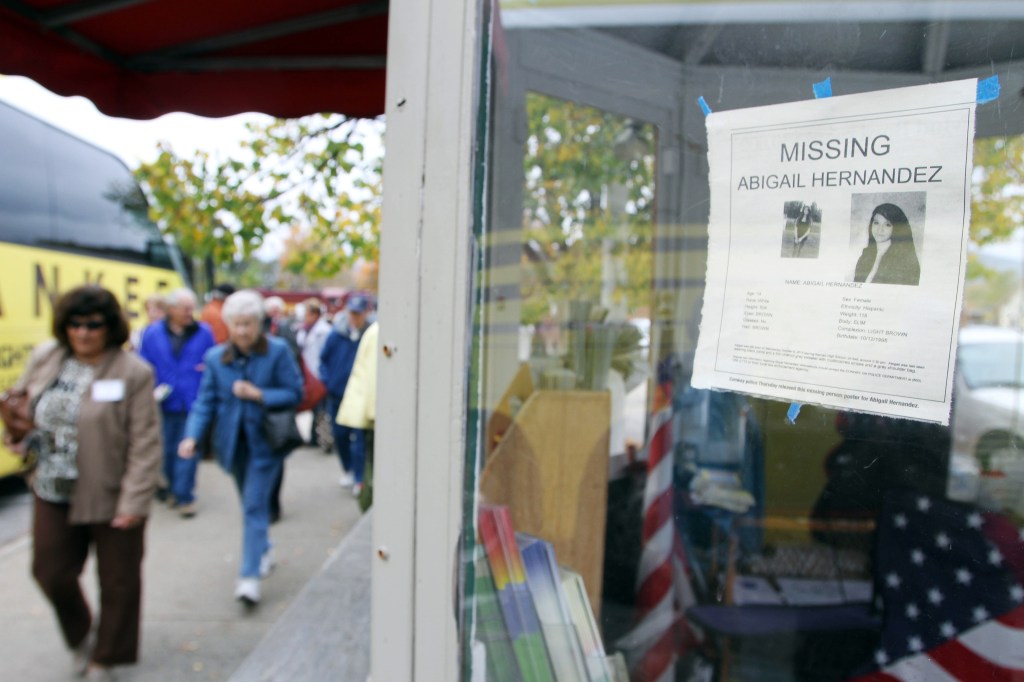 In this photo taken Wednesday Oct. 16, 2013, tourists walk by an information booth with a poster of missing teenager Abigail Hernandez in North Conway, N.H. Hernandez disappeared Wednesday Oct. 9 when she was last seen leaving school and walking towards home.