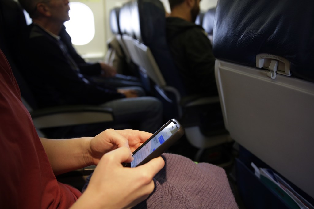 An airline passenger checks her cellphone before a flight Thursday in Boston. The Federal Aviation Administration’s new guidelines still don’t allow cellphone use at certain times.