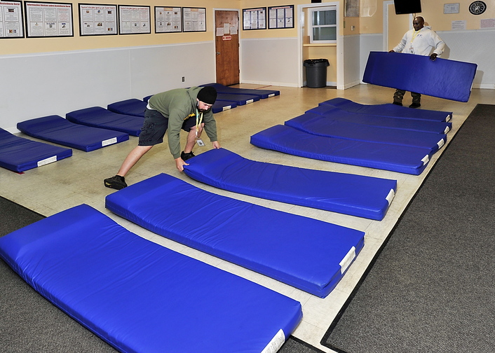 Gordon Chibroski/Staff Photographer Brian Marchant, left, and Bonane Rutijanwa, shelter attendants for Portland’s Oxford Street Shelter, arrange mats on the floor of the General Assistance Office Thursday for homeless people to sleep on if the other shelters are full.