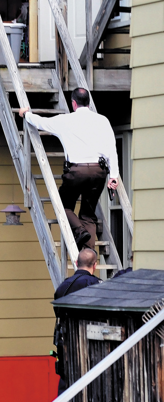 Detective David Caron, with his gun drawn, and other officers enter the second floor apartment at 90 Elm Street in Waterville on Wednesday.