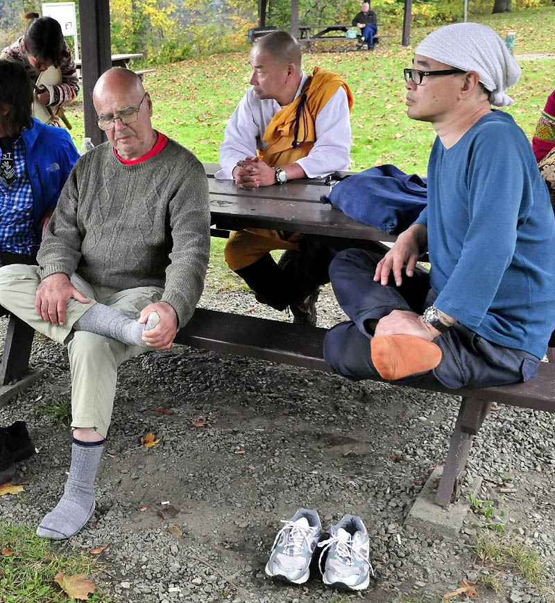 Marchers against the use of drone technology take a break on their march at the rest area along Route 2 in Skowhegan on Sunday. Jules Orkin, left, and Jiro Izuhara took off their shoes to rest their feet. Senji Kanaeda is at center.