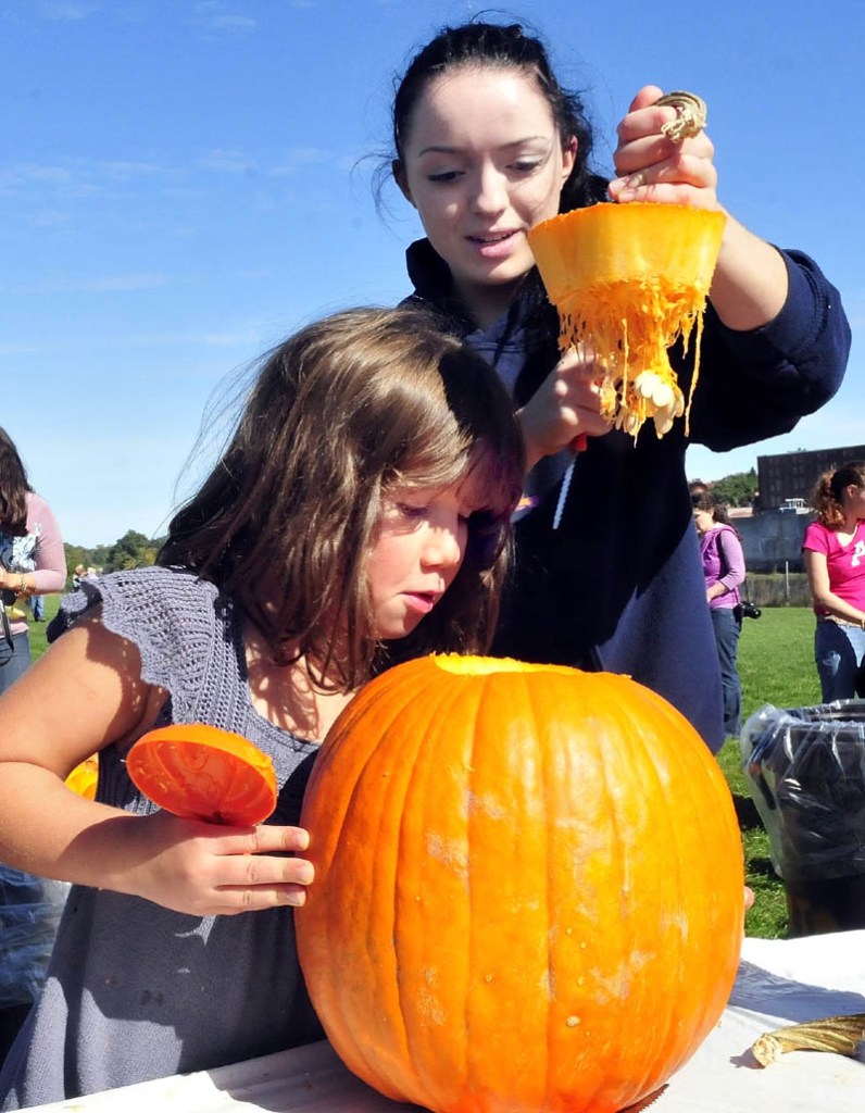 Colby College student Carmen Cordova lifts the top of a pumpkin that she cut as Kate Boudreau peers inside during the Harvest Fest in Waterville on Sunday.