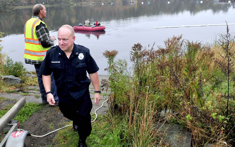 Pittsfield police officer Jeff Vanadestine walks back to his cruiser as firefighters search the Sebasticook River for debris and collect oils after a vehicle struck a nearby pole and went into the water on Monday. Vanadestine was one of the first at the scene and jumped into the water to rescue the female driver.