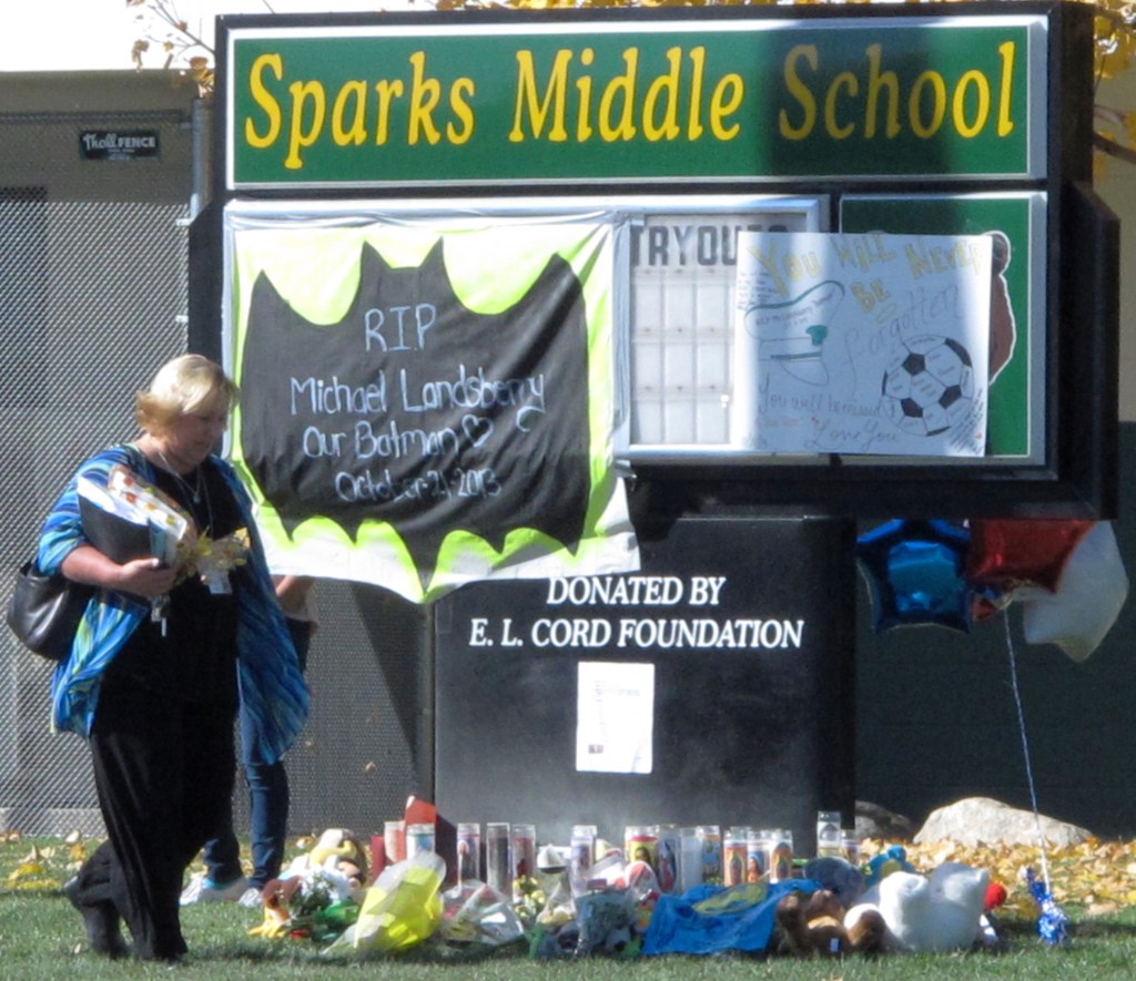 In this Oct. 23, 2013, photo, Washoe County School Board President Barbara Clark walks past a makeshift memorial in front of Sparks Middle School in Sparks, Nev., where math teacher Michael Landsberry was killed and two students wounded before a 12-year-old gunman killed himself.
