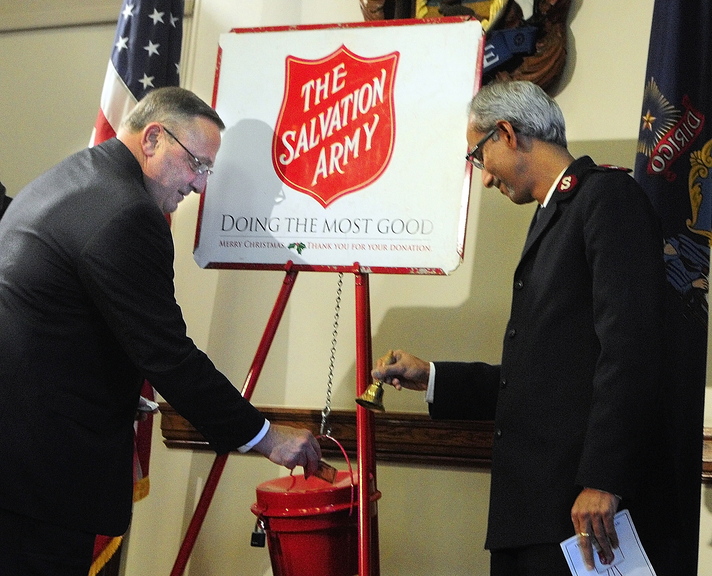 Kettle donation: Gov. Paul LePage, left, slips some cash into a Salvation Army kettle Thursday in the State House Cabinet Room in Augusta as Maj. Asit George, right, rings a bell. He and others from the Salvation Army were there for a statewide kettle kickoff. The Salvation Army has been using kettles annually to collect donations since 1891, according to a Salvation Army news release.