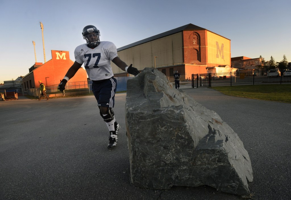 TOUCH THE ROCK: University of Maine football player Isaiah Brooks touches the rock at the entrance of Harold Alfond Sports Stadium in Orono before practice Wednesday. The rock has an upward pointing arrow painted on it, which signifies the Black Bears motto “One Direction.”