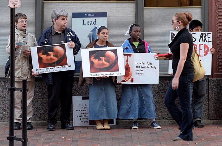 A pedestrian walks past anti-abortion protesters on Congress Street in Portland near the Planned Parenthood clinic on Oct. 4. Maine’s attorney general and her colleagues from 12 other states have signed onto a “friend-of-the-court” brief in support of protest-free buffer zones outside reproductive health clinics that provide abortions.