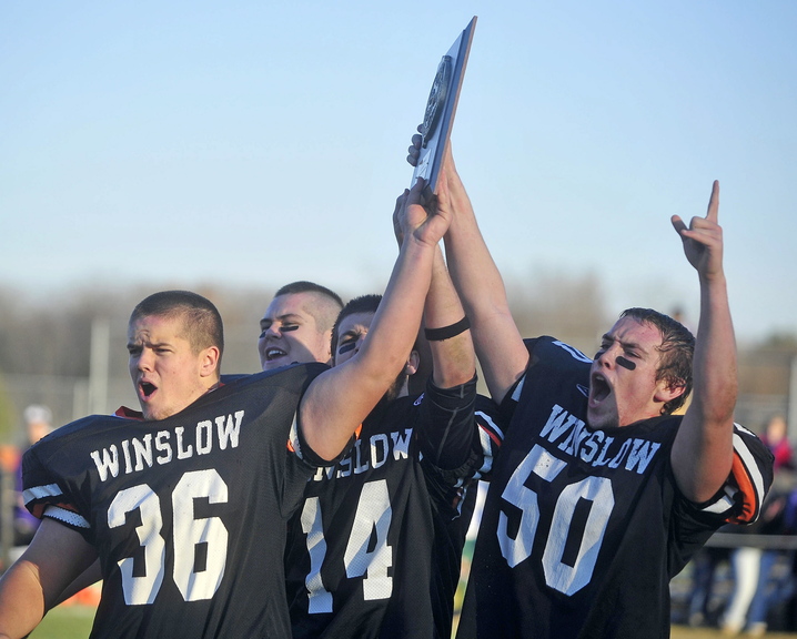Staff photo by Michael G. Seamans Winslow High School teammates Zach Guptill, 36, left, Troy Ellis, 79, back left center, Matt Fortier, 14, right center, and Tanner Gillliland, 50, right, hold up the Eastern Class C championship plaque after defeating Waterville Senior High School 49-12 in Winslow on Saturday.