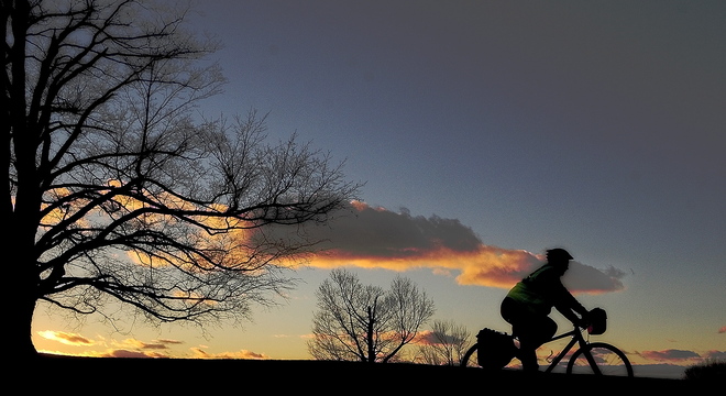 A cyclist rides north as the sun sets behind a tree on Tuesday on Hospital Street in Augusta.