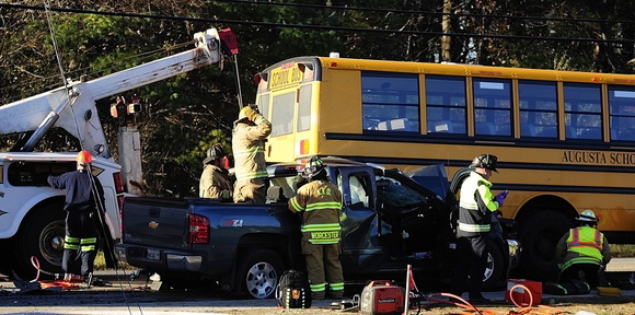 A tow truck driver lifts the bus off a pickup truck: as emergency crews work to free the pickup truck’s driver at the scene of a crash involving an Augusta school bus Tuesday on Riverside Drive, just south of Stevens Road, in Augusta.