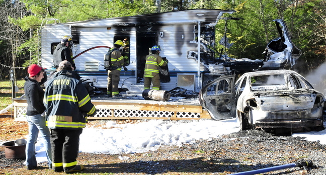 DESTROYED: Laura Ellis, left, speaks with a firefighter as others extinguish the destroyed remains of a camper she was staying in Tuesday on Beach Road in South China. Ellis was staying at friend and owner Tim Elkin’s camper when she started her car, right, which caught fire, then ignited the camper.