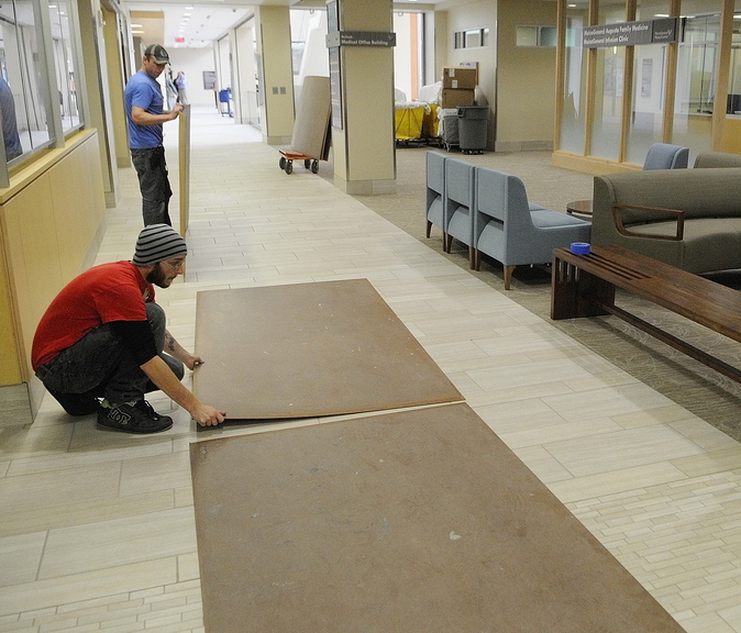 Zachary Curtis, bottom left, and James Ludlow put down boards over the tile in the front hallway on Friday to make it a smoother ride for stretchers that will be rolling through when patients are moved in at the Alfond Center for Health in Augusta.
