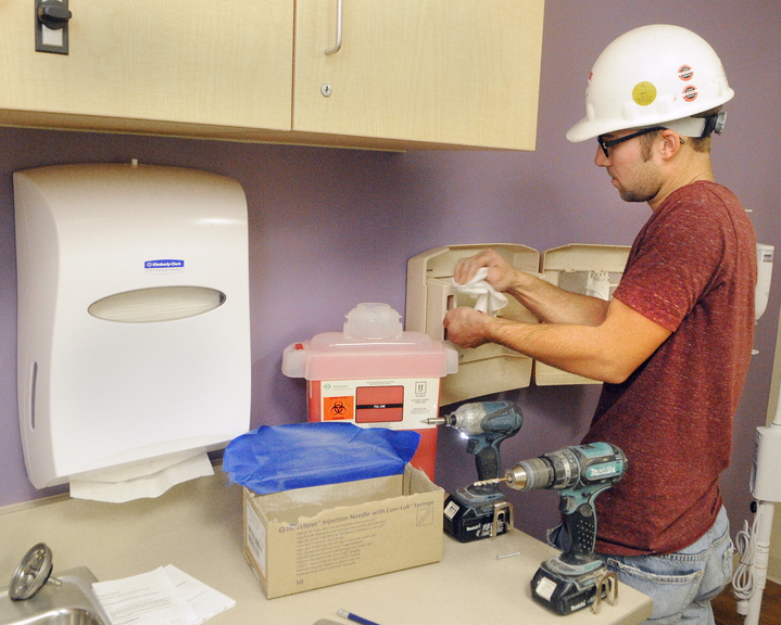 Aaron O’Neil wipes off dust from drilling in screws on Friday as he installs a sharps container at the Alfond Center for Health in Augusta. O’Neil and other H.P. Cummings employees were taking care of the last punch list items the day before the move.