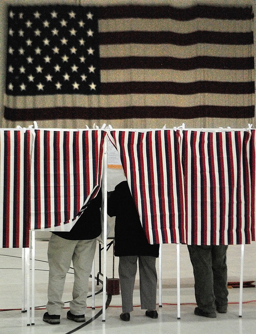 Voters fill in ballots in booths in front of a large American flag on Tuesday at Augusta’s Ward 1 polling place in the Augusta Armory.