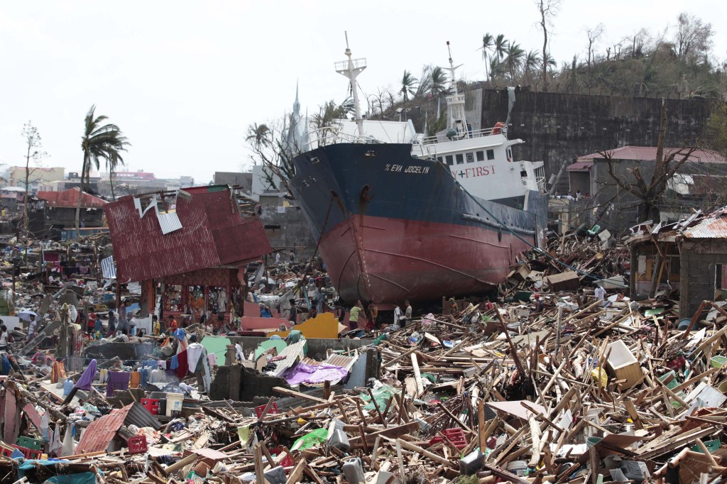 Survivors walk past a ship that lies on top of damaged homes after it was washed ashore in Tacloban city, Leyte province central Philippines on Sunday, Nov. 10, 2013. The city remains littered with debris from damaged homes as many complain of shortage of food, water and no electricity since the Typhoon Haiyan slammed into their province. Haiyan, one of the most powerful typhoons ever recorded, slammed into central Philippine provinces Friday leaving a wide swath of destruction and scores of people dead.