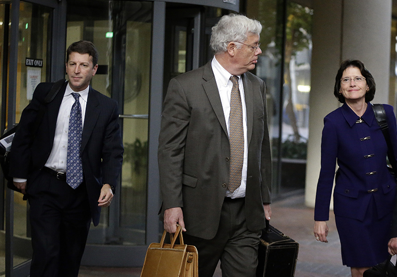 Harold McIlhenny, center, an attorney representing Apple Computer in the Apple Samsung trial, exits a federal courthouse Wednesday, Nov. 13, 2013, in San Jose, Calif. How much does Samsung Electronics owe Apple for copying vital features of the iPhone and iPad, such as scrolling and the "bounce-back" function at the end of documents? Apple says $380 million. Samsung counters with $52 million. The companies made their demands Wednesday during opening statements of a patent trial. At issue are 13 older products a previous jury found infringed several Apple patents. That previous jury awarded Apple $1.05 billion after determining 26 Samsung products had infringed six Apple patents.