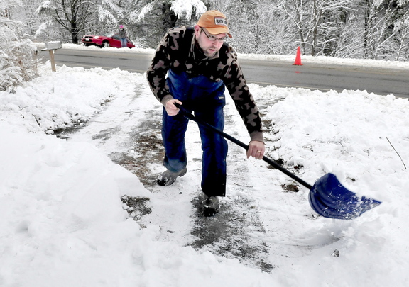 WINTER WOES: Don Gardner clears his driveway in Sidney as motorist Lydia Williams, in background, waits for a tow truck after her car slid off the snow-covered West River Road on Monday.