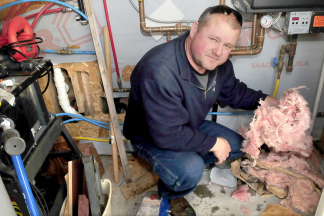 DAMAGE: Inside a furnace room in Jean Mosher’s home in Smithfield, her son Andrew Landry holds insulation that he said rats from a neighbor’s pig farm pulled from a wall. At left are holes in the walls that were made to gain access to repair pipes damaged by the rats.