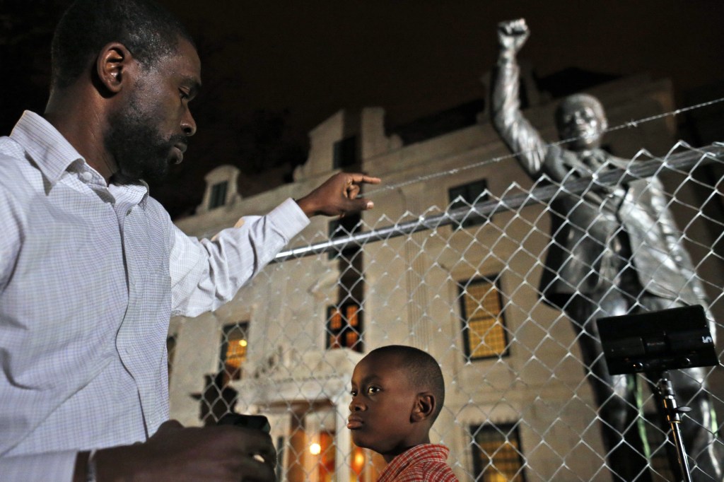 Dijon Anderson of Bowie, Md., and his son Keaton, 10, visit the statue of Nelson Mandela at the South African Embassy in Washington, which is currently under renovation, Thursday, Dec. 5, 2013. Mandela, former President of South Africa and anti-apartheid icon, died earlier Thursday at 95.