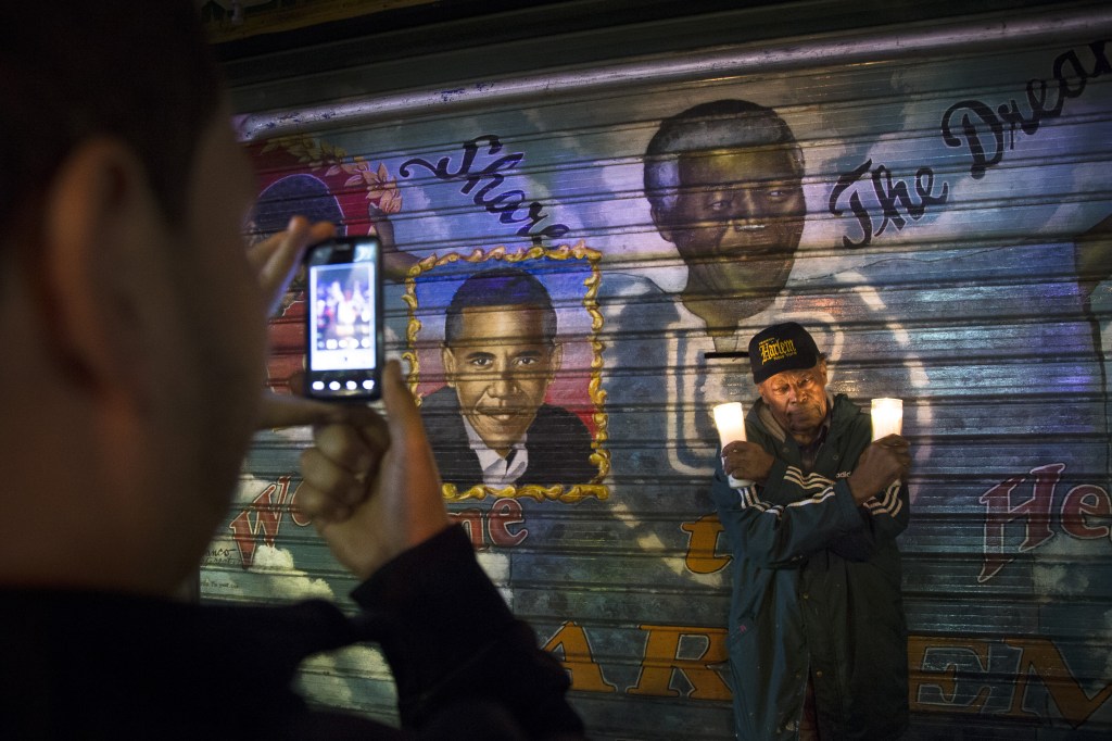 A man takes a picture of an artist who goes by the name “Franco the Great” in front of a mural of South African leader Nelson Mandela that the artist painted in 1995, and later added U.S. President Barack Obama, on 125th Street in the Harlem neighborhood of New York, Thursday, Dec. 5, 2013. Mandela, South Africa’s first black president, died Thursday after a long illness. He was 95.