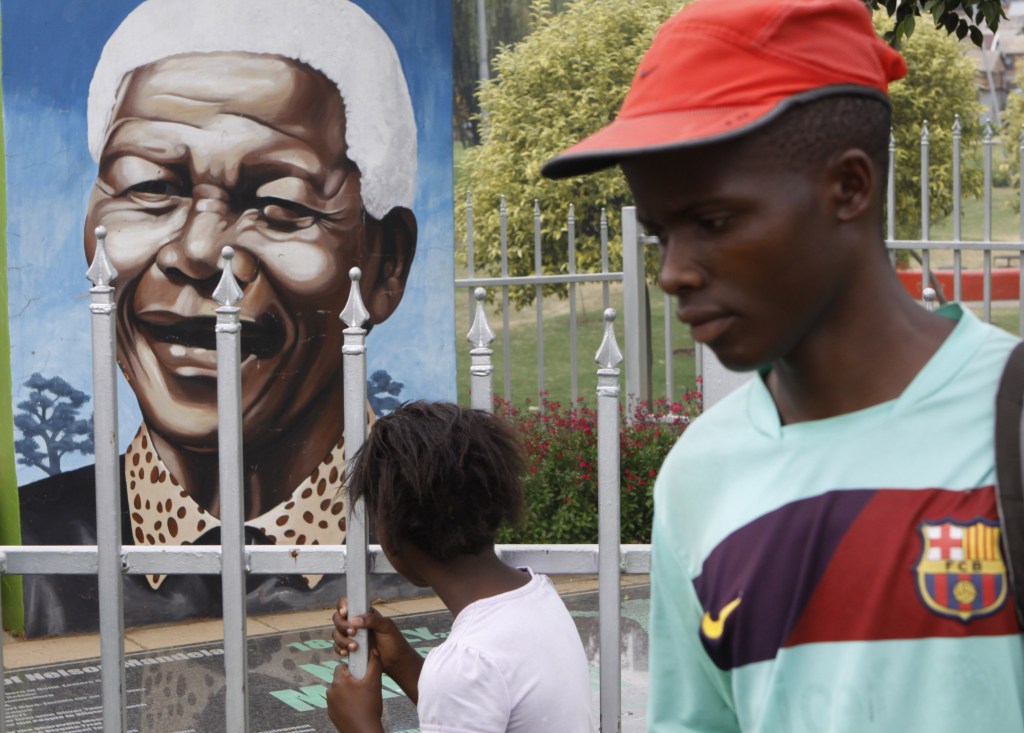 A child looks through a fence at a portrait of former President Nelson Mandela in a park in Soweto, South Africa, in this March 28, 2013 file photo. The Nobel laureate is a revered figure in South Africa, which has honored his legacy of reconciliation by naming buildings and other places after him and printing his image on national banknotes. On Thursday, Dec. 5, 2013, Mandela died at the age of 95.