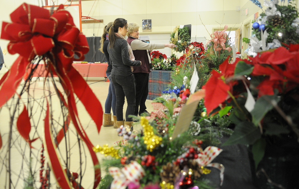 AUCTION ARRANGEMENTS: Val Dawes, right, plans the auction of floral arrangements Sunday with fellow volunteers Quinn Galletta, center, and Mair Guillemette at the Manchester Elementary School. The annual auction raises funds for winter home heating relief for Manchester residents.