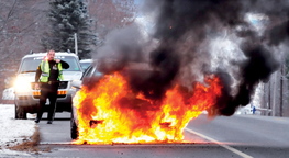 On fire: Fairfield Police Sgt. Paul St. Amand monitors a car that burst into flames on Norridgewock Road on Tuesday.