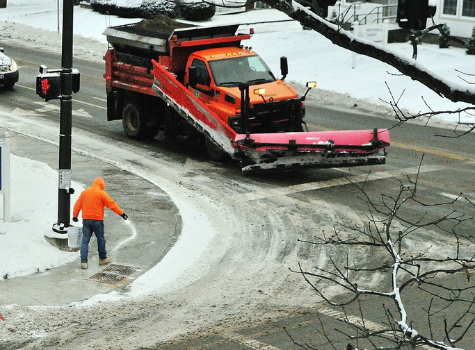 A person scatters salt on the sidewalk next to a City of Augusta snowplow at the corner of Capitol and Sewall Streets on Tuesday in Augusta. People were out across the region with all types of snow removal gear.