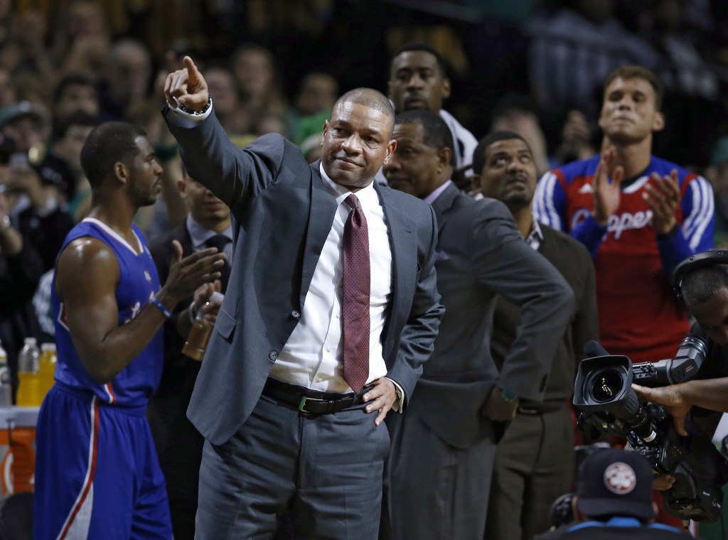 Current Los Angeles Clippers head coach and former Boston Celtics head coach Doc Rivers acknowledges fans during a video tribute to him in his first time back to the TD Garden after the first quarter of an NBA basketball game in Boston, Wednesday, Dec. 11, 2013. Applauding are Clippers Chris Paul, left, and Blake Griffin, far right. (AP Photo/Elise Amendola)