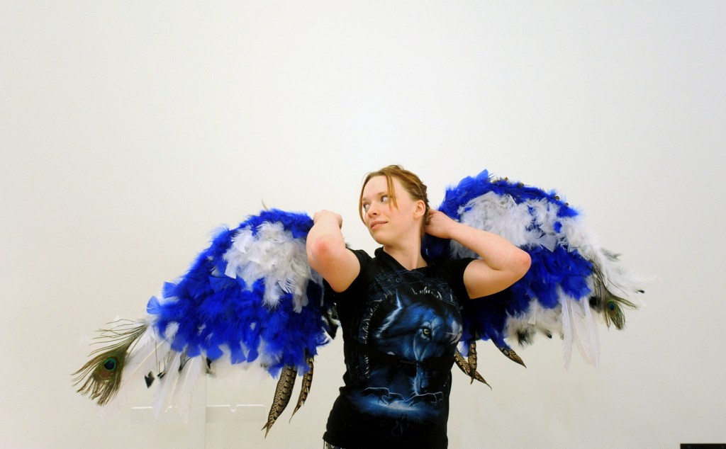 Wings: Maeve-Wolf O’Reiley, 21, a sculpture student at the University of Maine at Farmington, tries on her prosthetic creation titled “Flights of Fantasy” during a set-up Wednesday for the campus exhibition. O’Reiley used more than 700 feathers and spent more than two weeks creating the winged prosthesis.