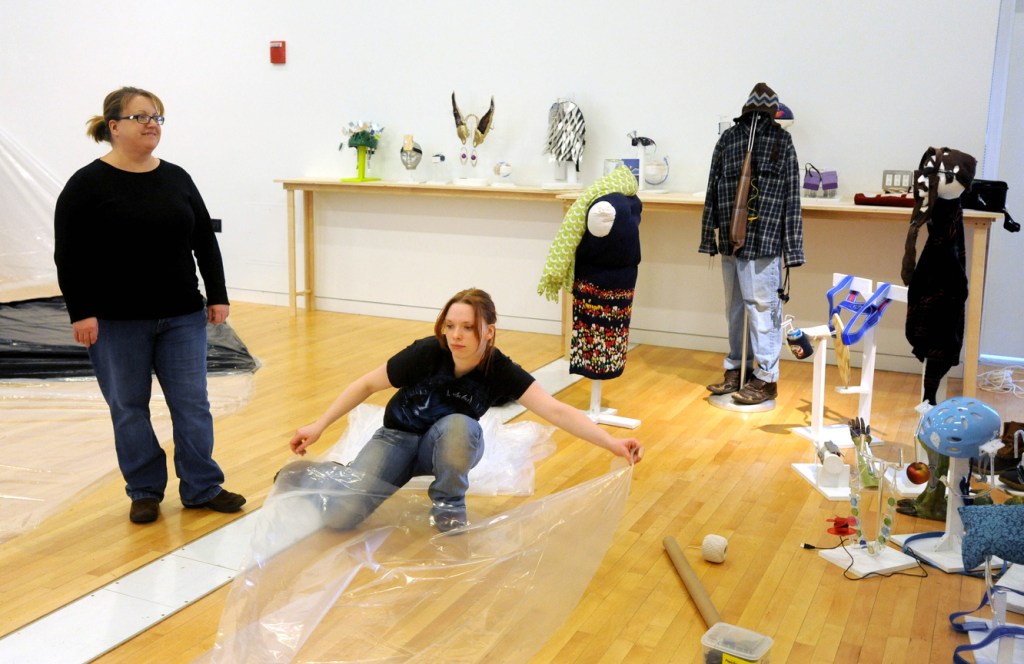 PROSTHESIS ART: Maeve-Wolf O’Reiley, center, and Jill Gingras, left, both sculpture students at the University of Maine at Farmington, prepare the Emery Arts Center for the prosthesis project on Wednesday. Students were challenged to create a prosthesis to overcome their own personal limitations.