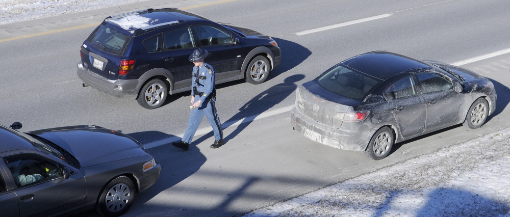 SAFETY FIRST: A car drives past Maine State Trooper Chris Rogers during a traffic stop Thursday in West Gardiner. Several State Police cruisers have been struck while parked at accidents this year, compelling police to remind drivers that they must slow down and pull over when approaching emergency vehicles.