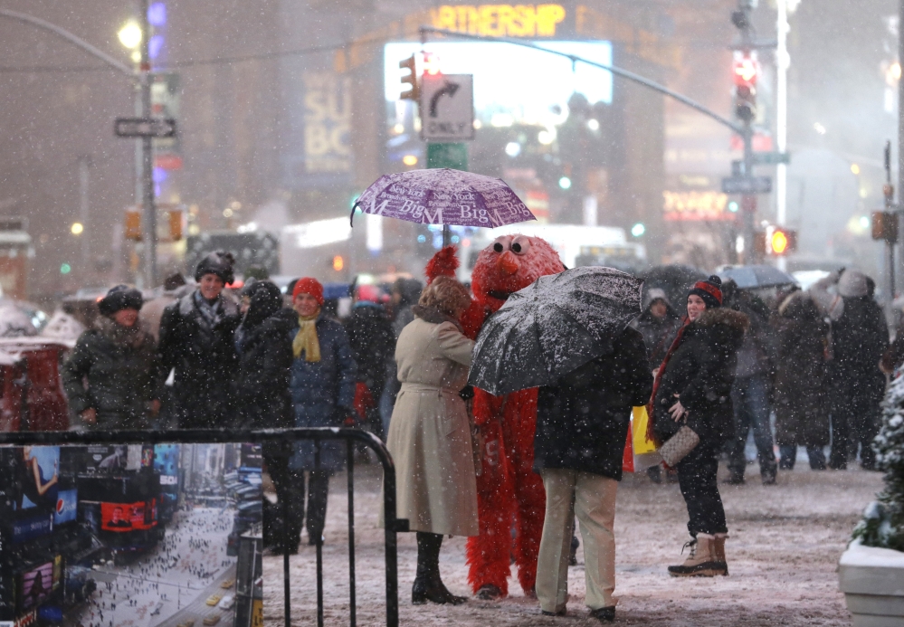 A person wearing an Elmo outfit holds an umbrella for a woman as she searches for money to give to the character after posing for a photo together at Times Square, Saturday, Dec. 14, 2013, in New York. Manhattan is experiencing heavy snow with reports saying the weather will continue to cover the city with snow throughout the night.