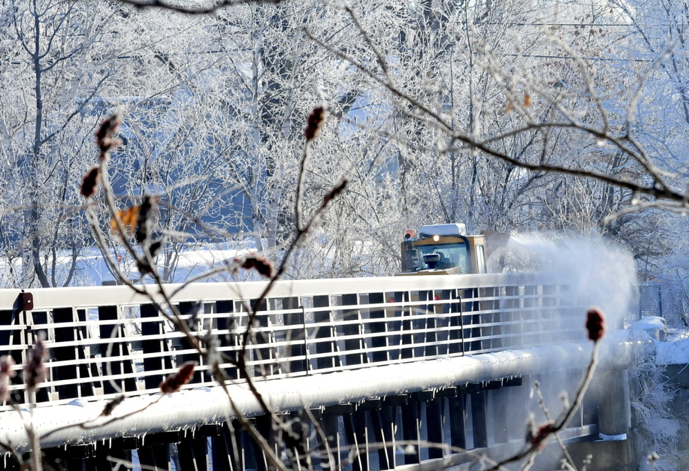 ICY COLD: A Skowhegan Highway Department snowblower clears snow from the ice-covered walking bridge on Tuesday. Freezing spray from the Kennebec River covered nearby tree limbs with ice.