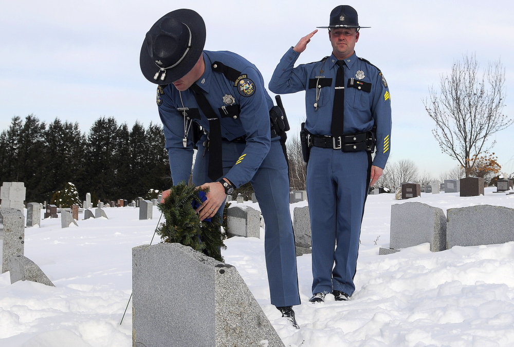 Maine State Police Sgt. Bruce Scott salutes as Trooper Elisha Fowlie lays a wreath Tuesday on the headstone of Trooper Michael Veilleux at St. Mary’s Cemetery in Manchester. During a memorial service Tuesday, wreaths were placed on the headstones of 11 state police troopers who died in the line of duty. Organizers hope that the service will be an annual tradition, State Police Lt. Scott Ireland said. Retired troopers and friends of Veilleux remembered the 24-year-old who was killed in a car accident in Dayton in 1986.