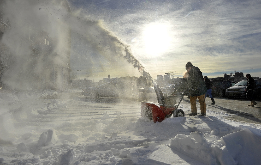 An employee uses a snowblower to clear the parking lot at the Department of Health and Human Services on on Marginal Way in Portland on Tuesday, just in time for more snow that is headed for Maine.