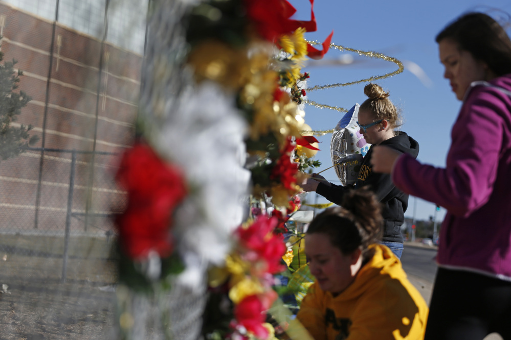 Arapahoe students leave flowers and other items at a makeshift tribute site three days after a shooting attack at Arapahoe High School in Centennial, Colo., Monday, Dec. 16, 2013. They are from left, Hannah Eddy, at bottom, Gavyn Bills, and Vania Arevalo. During the attack, the shooter shot a classmate in the head at close range with a shotgun, before killing himself.