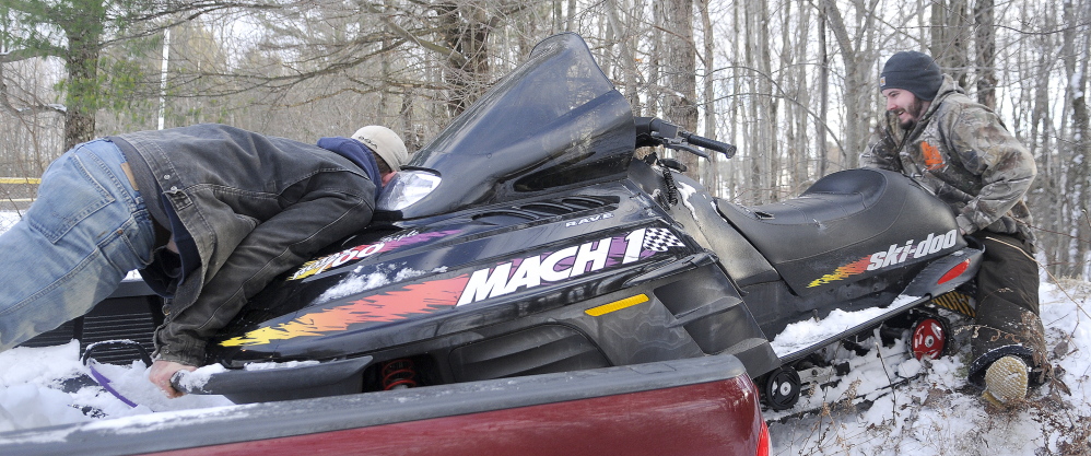 REVERSE: Josh Grant, left, pushes as Blake Cahill pulls a snowmobile off the bed of his pickup truck in Hallowell Wednesday. Cahill had just bought the machine and was taking it for an inaugural ride on the trails through the city.