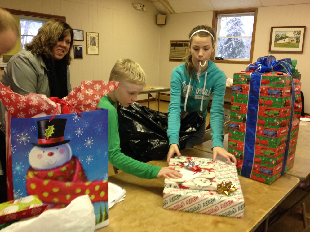 Christmas spirit: Ryan Gray, 8, left, and Olivia Bourque, 12, help distribute donated gifts to Maine Department of Health and Human Services caseworkers Monday morning at Sacred Heart Parish Hall in Hallowell. The presents, largely bought by parishioners of three Hallowell churches, will be given to families in need before Christmas.