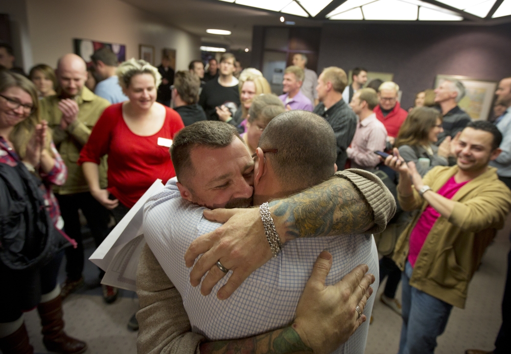 Chris Serrano, left, and Clifton Webb embrace after being married, as people wait in line to get licenses outside of the marriage division of the Salt Lake County Clerk’s Office in Salt Lake City. A federal judge is set to consider a request from the state of Utah to block gay weddings that have been taking place since Friday when the state’s same-sex marriage ban was overturned.