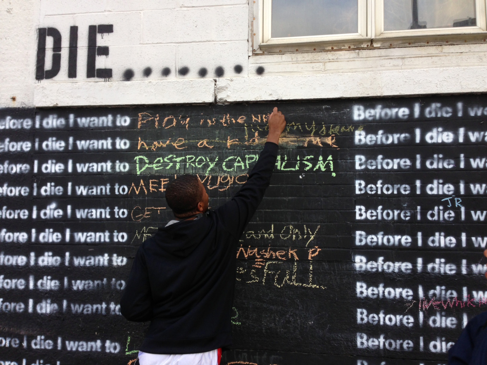 Nyquis Turner, 16, writes “Play in the NFL” on a wall in Syracuse, N.Y., that invites passers-by to complete the sentence: “Before I die, I want to...”