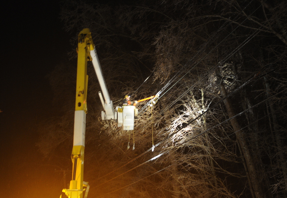 POWER UP: An employee of electrical contractor Coutts Brothers hangs a power line Monday night in Hallowell. Thousands across Maine remain without power because of an ice storm that coated lines and limbs.
