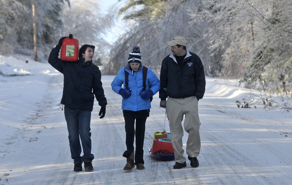 Staff photo by Michael G. Seamans STORM RECOVERY: Chris Devine, far right, hauls a sled of gifts with his daughter Jordan, 11, and step son Derek Gervais, 20, far left, carrying gas for the generator on Maplehurst Lane in Belgrade on Wednesday, Dec. 25, 2013. The Devine's lost power on Monday and haul their supplies in on sled. Trees and power lines are down on both sides of their driveway essentially making it impossible to drive in. Luckily they weren't home when the trees fell during the storm affording them the opportunity to drive to town for gas and other essentials for life off the grid.