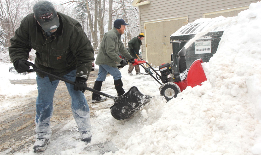 A TEAM EFFORT: Steve Schmidt, center, along with Scott Berry, left, and Ryan Doyon, far right, work to clear a parking lot behind an apartment building owned and operated by Kennebec Behavioral Health on Silver Street in Waterville on Monday. Sunday night’s fast-moving storm dumped close to a foot of snow in many locales in central Maine.