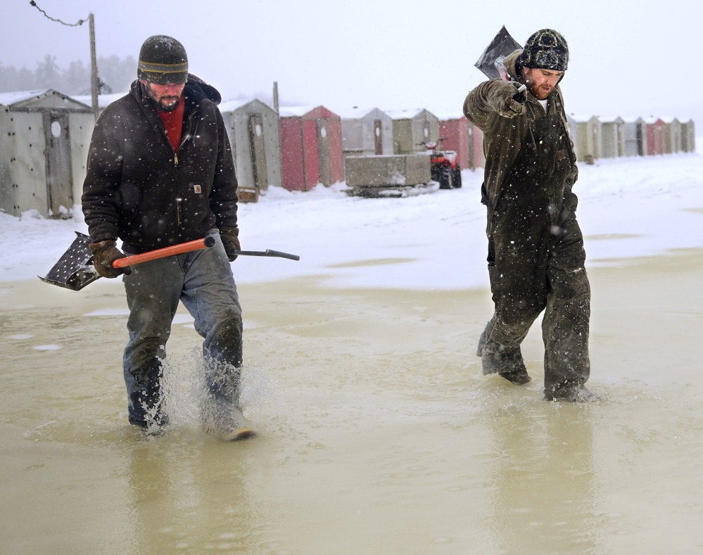 FISHING TIME: Mike Abbott, left, and Brandon Sutherburg walk through tidal slush to shore Thursday at Baker’s Smelt Camps in Pittston. The men had broken open frozen race holes and cleaned the camps on the Kennebec River in sub-zero temperatures.