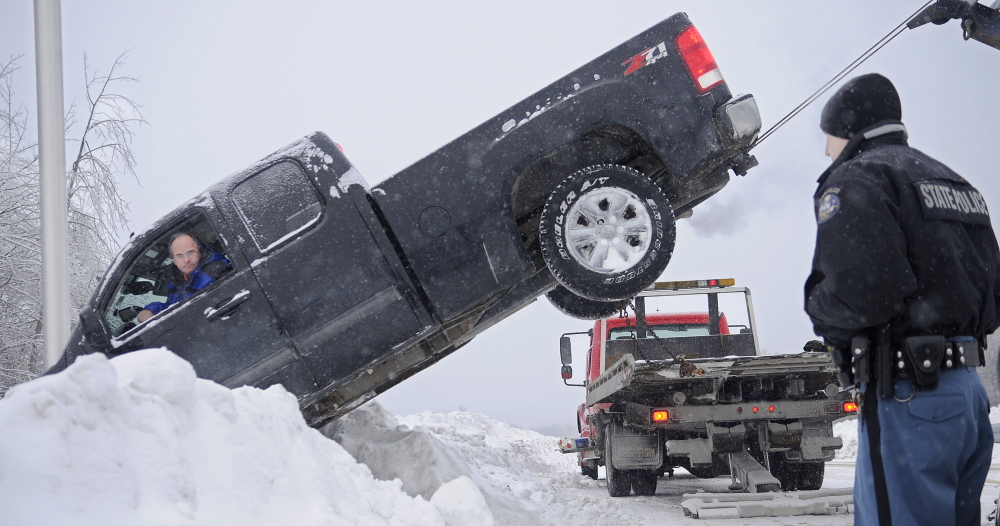 HIGH AND TIGHT: State Trooper Chris Rogers watches as AC Towing pulls a pickup driven by Paul Dubois of Madawaska over a guardrail Thursday at the on-ramp for the northbound lane of Interstate 295 in Gardiner. Dubois’ vehicle came to rest several feet down a steep embankment after going over a guardrail in the snow, Rogers said. Two wreckers from AC Towing worked for more than an hour in sub-zero temperatures to pull the pickup back onto the road. Dubois was not injured.