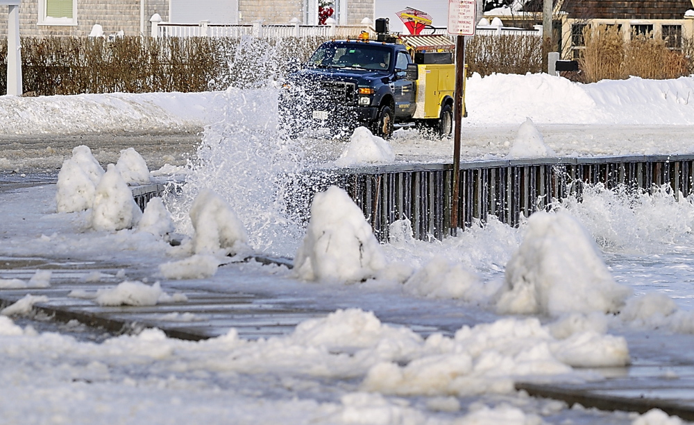 Eric Cloutier, an employee of the Kennebunk area water district, braves the waves splashing over the road as he heads for a water pipe break at one of the residences along the ocean. The road was closed to all but local traffic and workers.