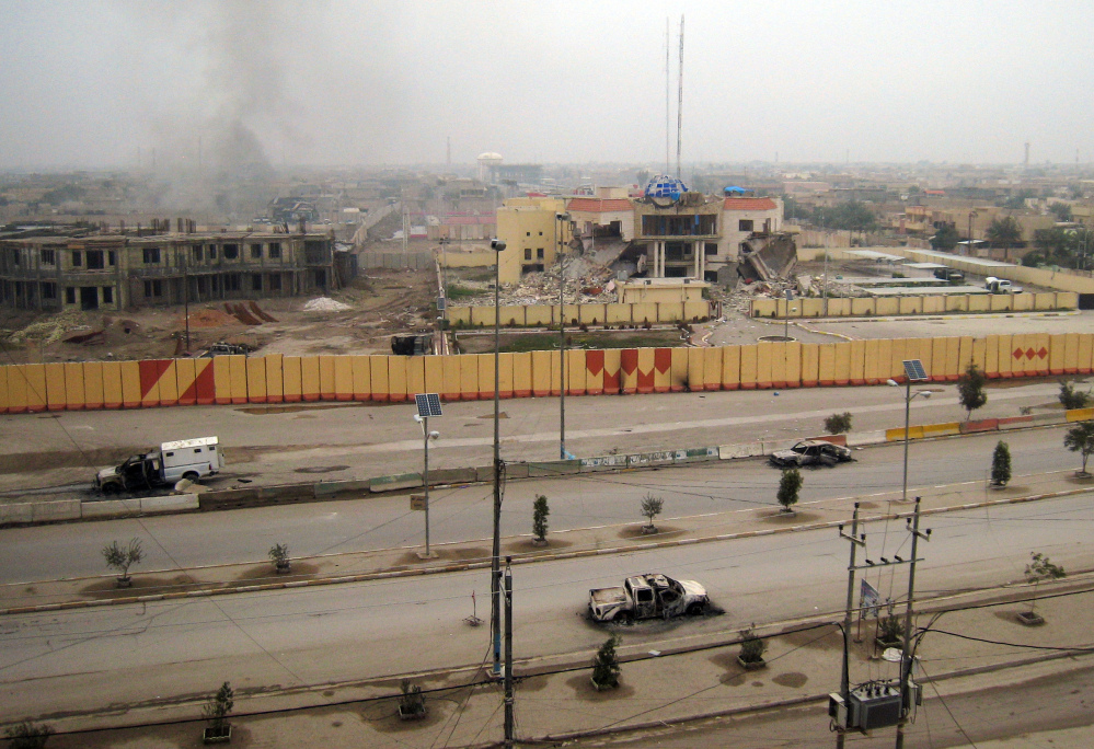 Burned vehicles litter an empty street, and buildings, including a provincial government building, center in the background, show damage in Fallujah, 40 miles west of Baghdad, Iraq, on Friday.